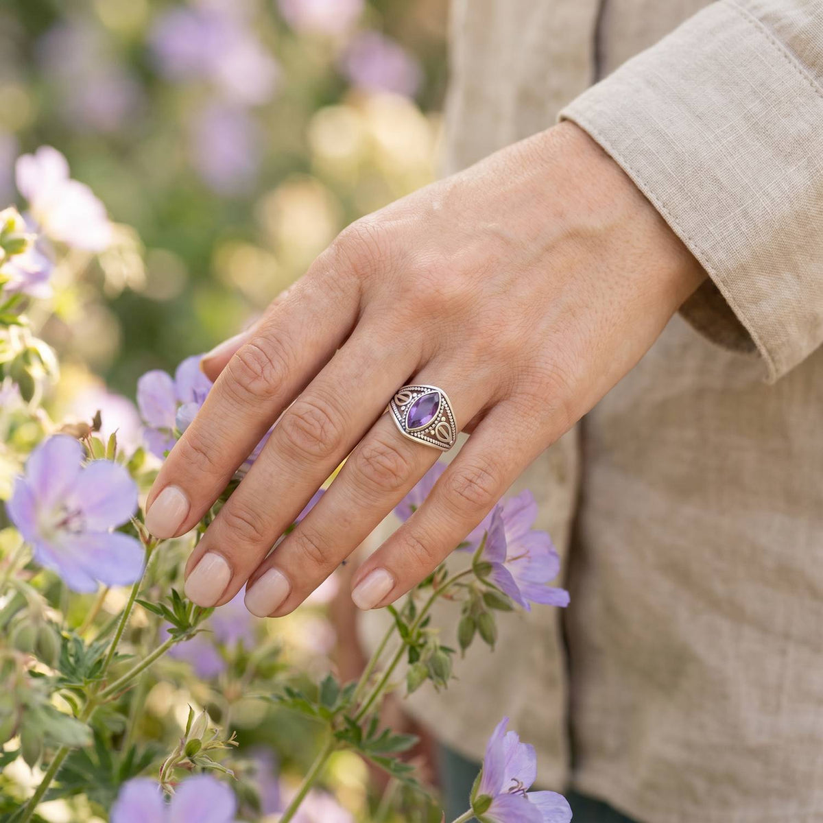 Silberring mit Amethyst an der Hand zwischen Blumen