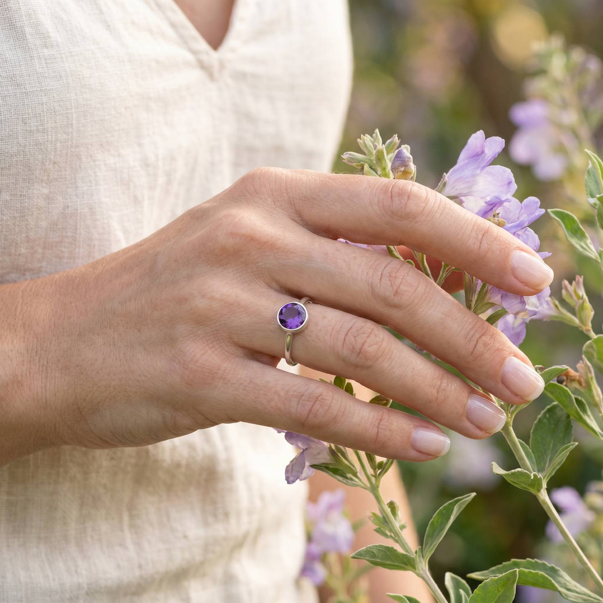 Silberring mit Amethyst an der Hand zwischen Blumen