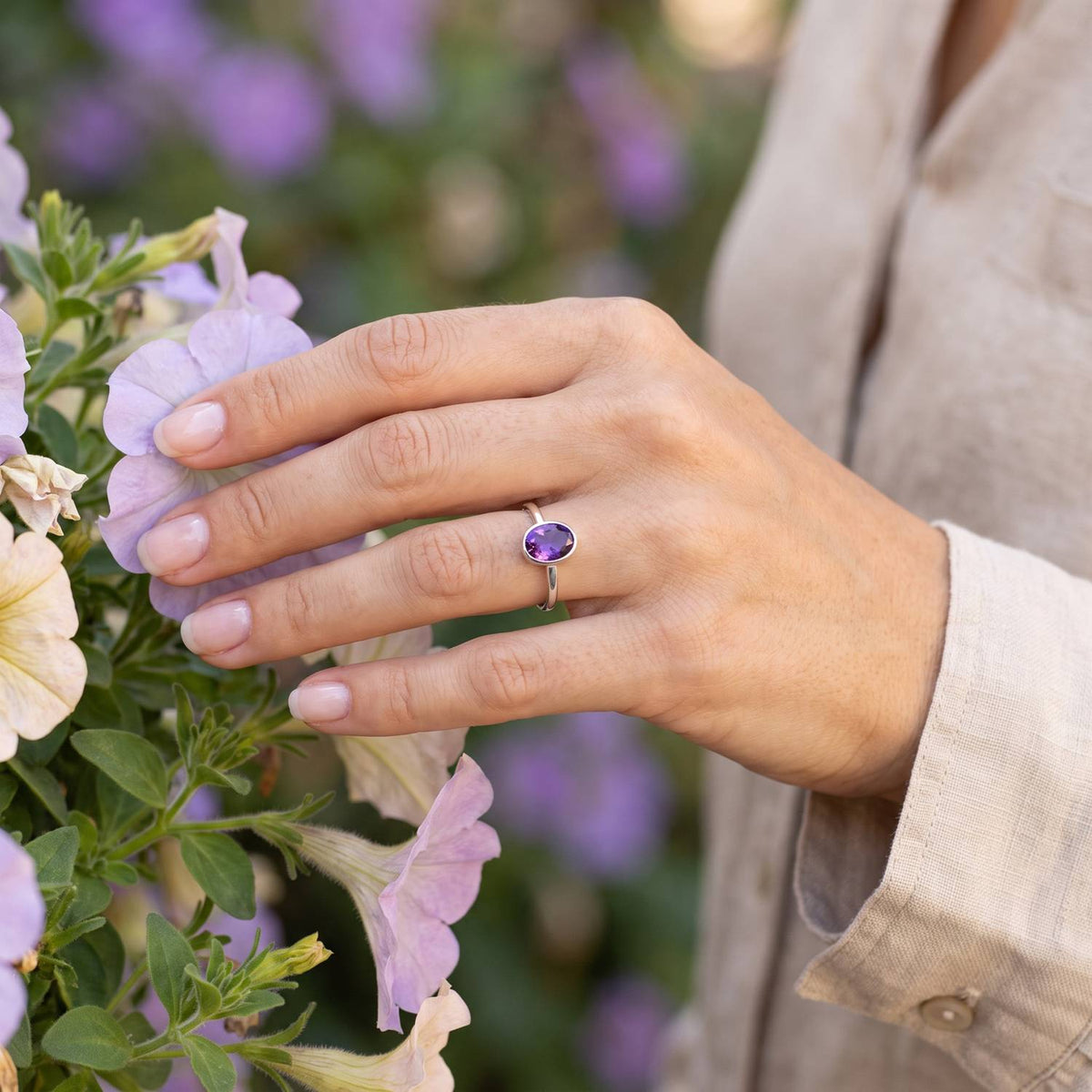 Silberring mit Amethyst an der Hand zwischen Blumen