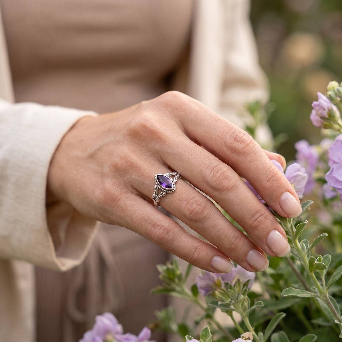 Silberring mit Amethyst an der Hand zwischen Blumen