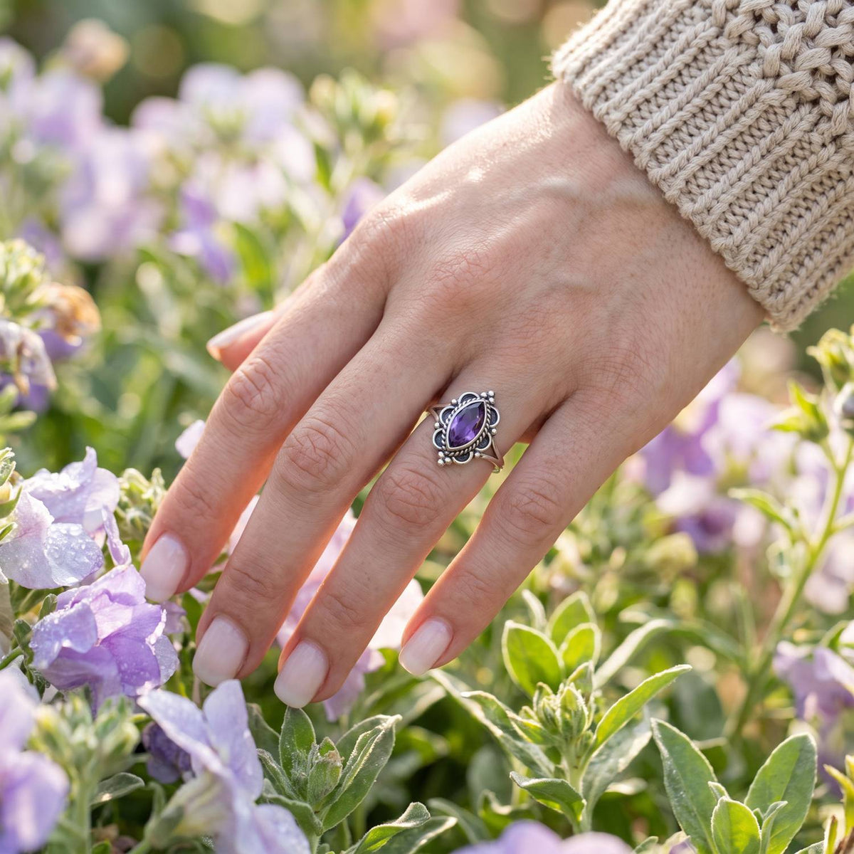 Silberring mit Amethyst an der Hand zwischen Blumen
