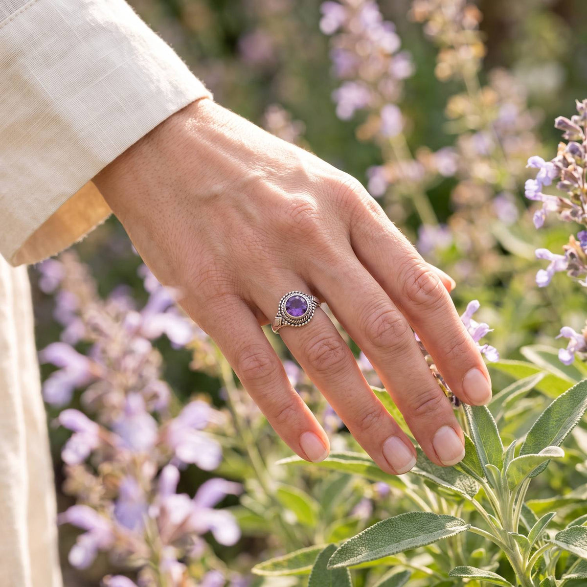 Silberring mit Amethyst an der Hand zwischen Blumen