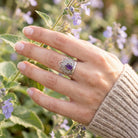 [KI] Silberring mit Amethyst an der Hand zwischen Blumen