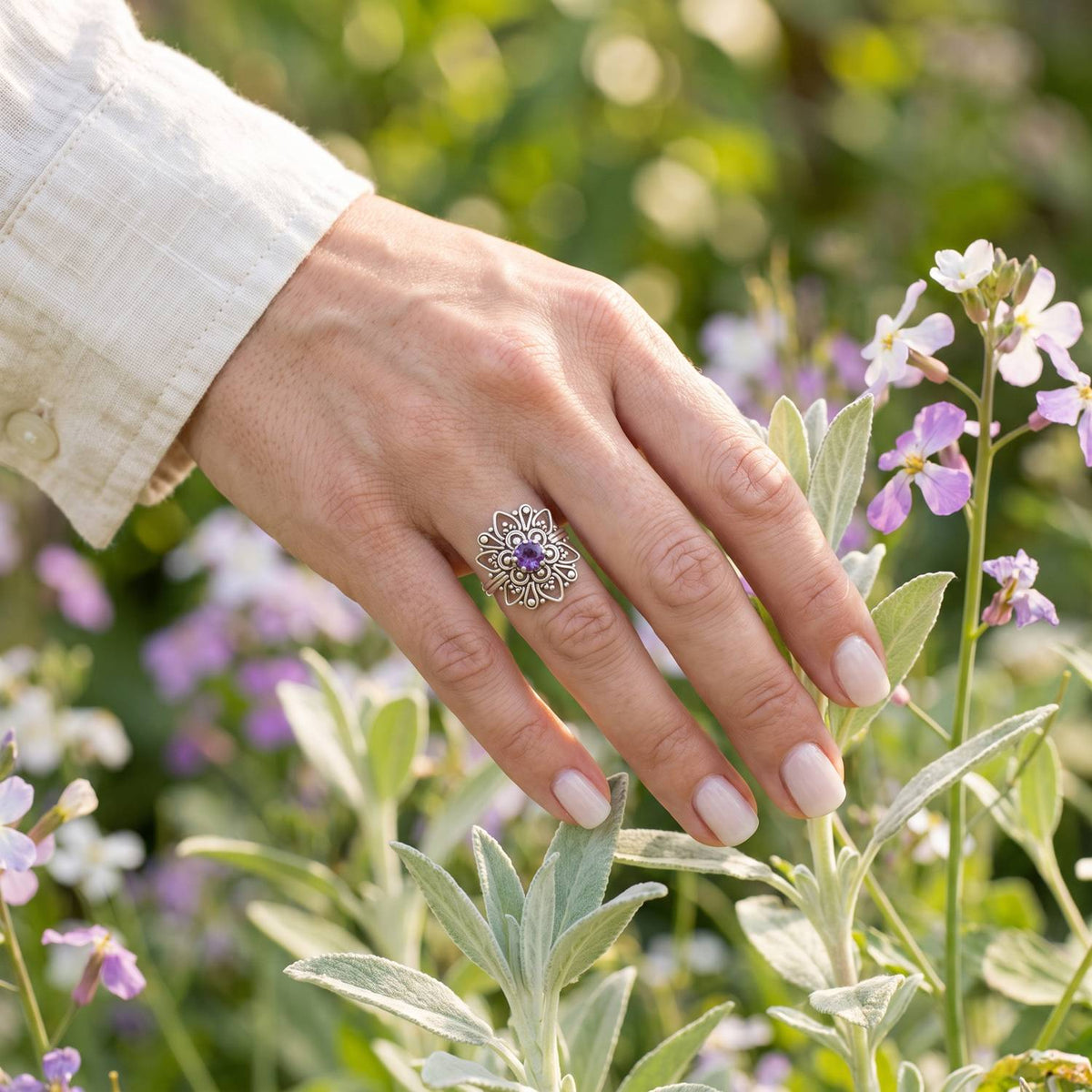 Silberring mit Amethyst an der Hand zwischen Blumen