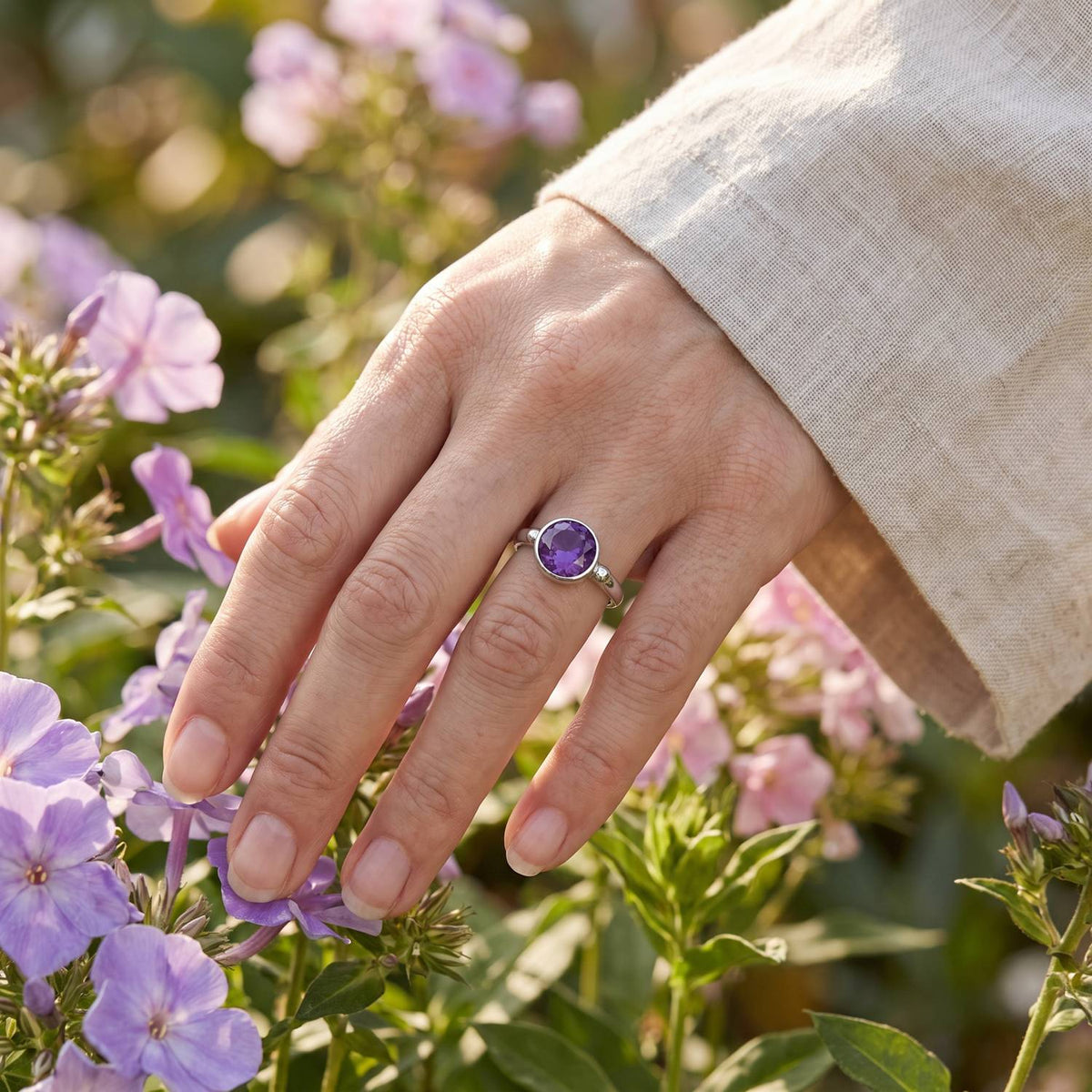 Silberring mit Amethyst an der Hand zwischen Blumen