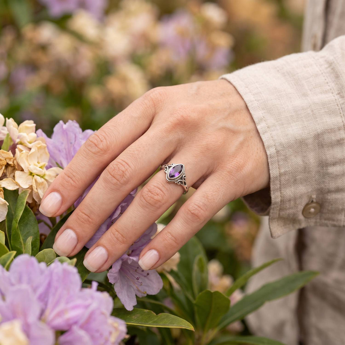 Silberring mit Amethyst an der Hand zwischen Blumen