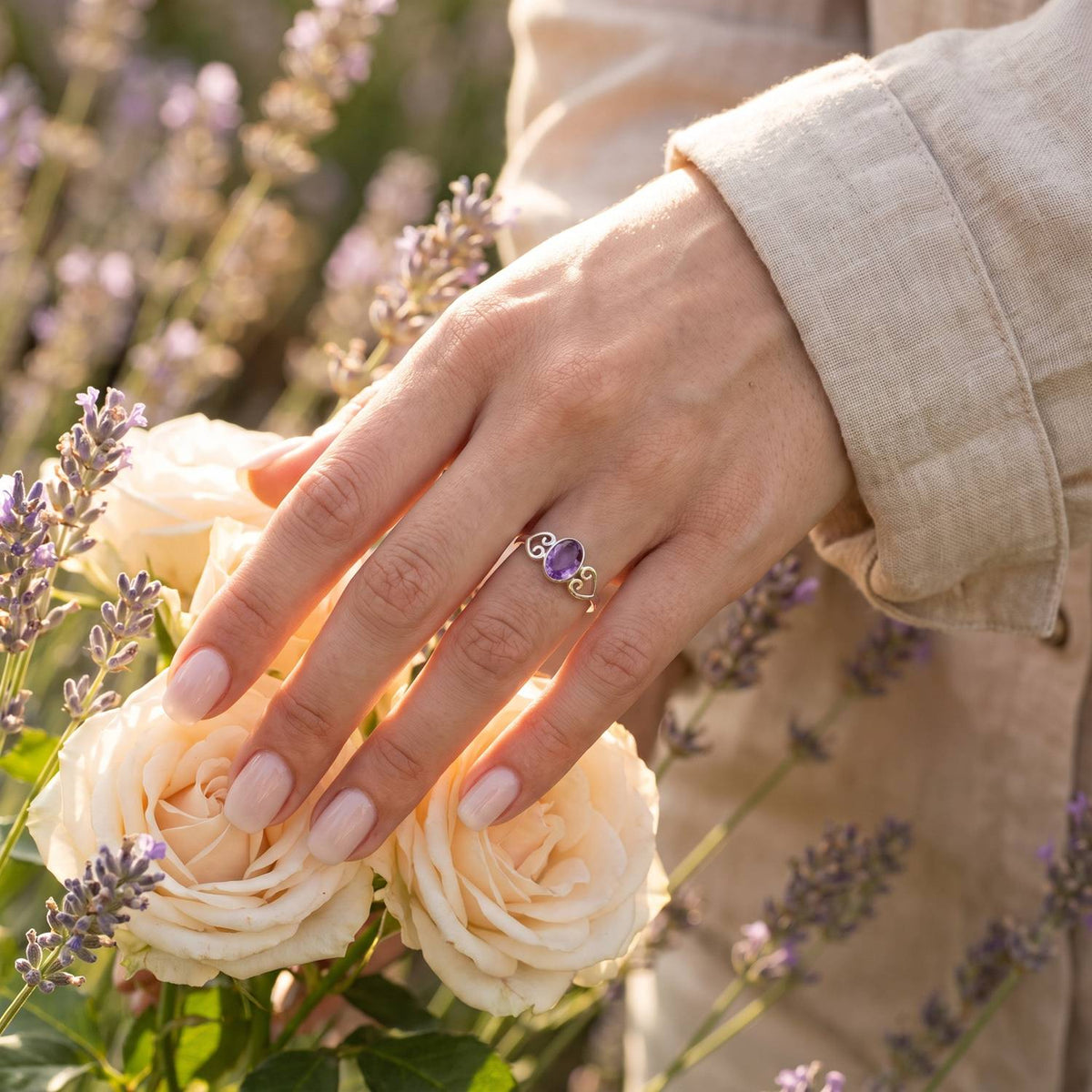 Silberring mit Amethyst an der Hand zwischen Blumen