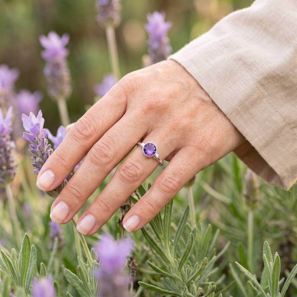 Silberring mit Amethyst an der Hand zwischen Blumen
