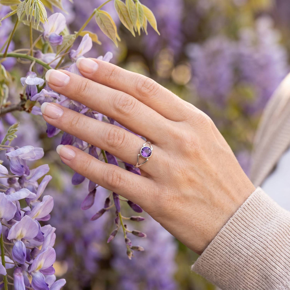 Silberring mit Amethyst an der Hand zwischen Blumen