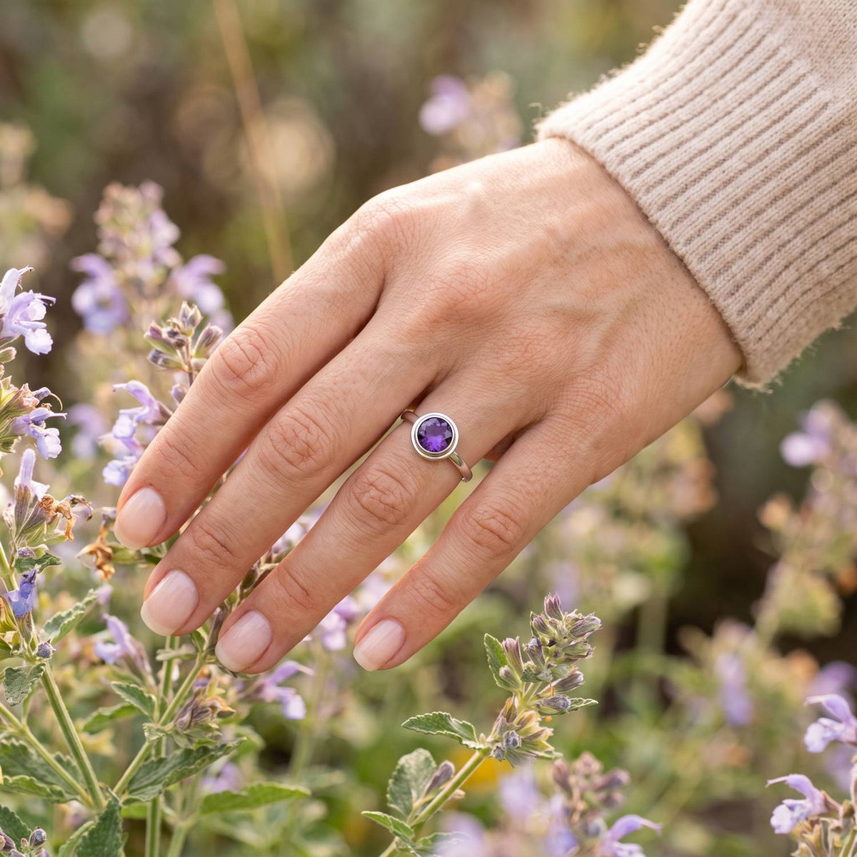 Silberring mit Amethyst an der Hand zwischen Blumen