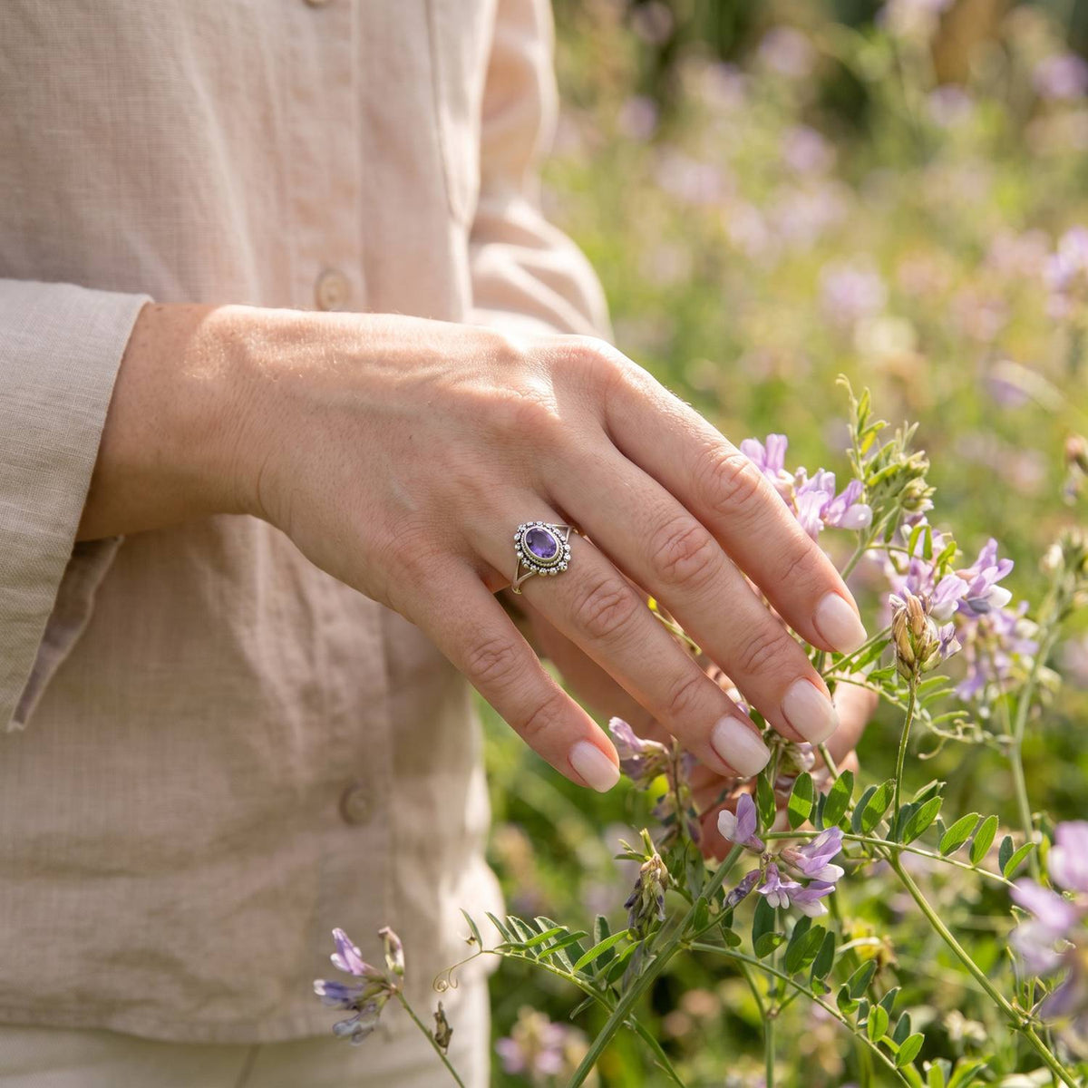 Silberring mit Amethyst an der Hand zwischen Blumen