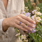[KI] Silberring mit Amethyst an der Hand zwischen Blumen