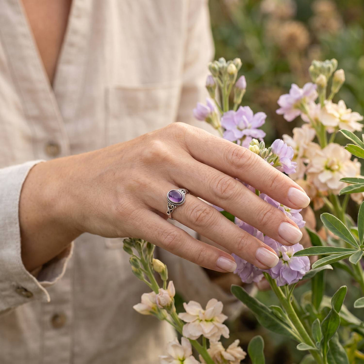 Silberring mit Amethyst an der Hand zwischen Blumen
