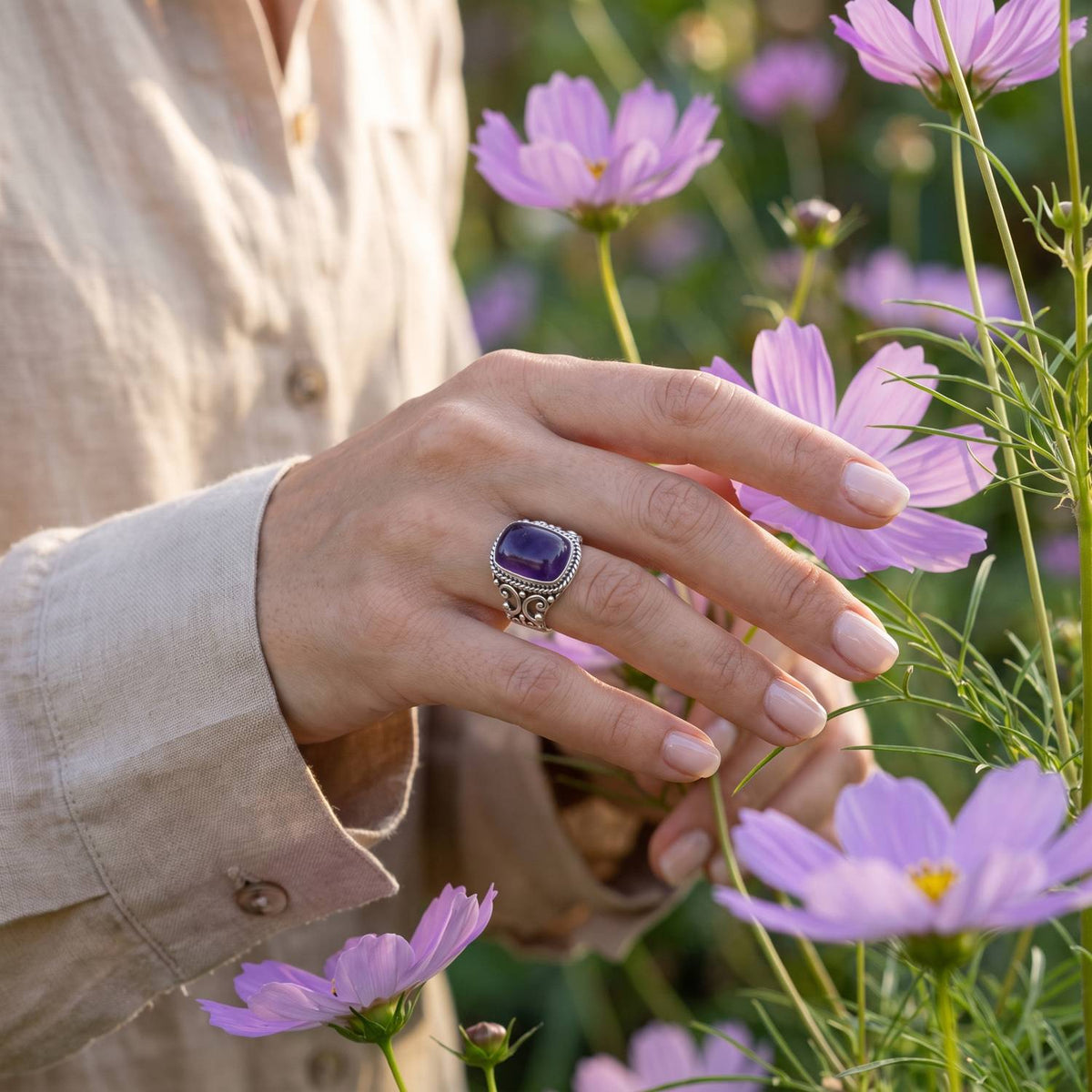 Silberring mit Amethyst an der Hand zwischen Blumen