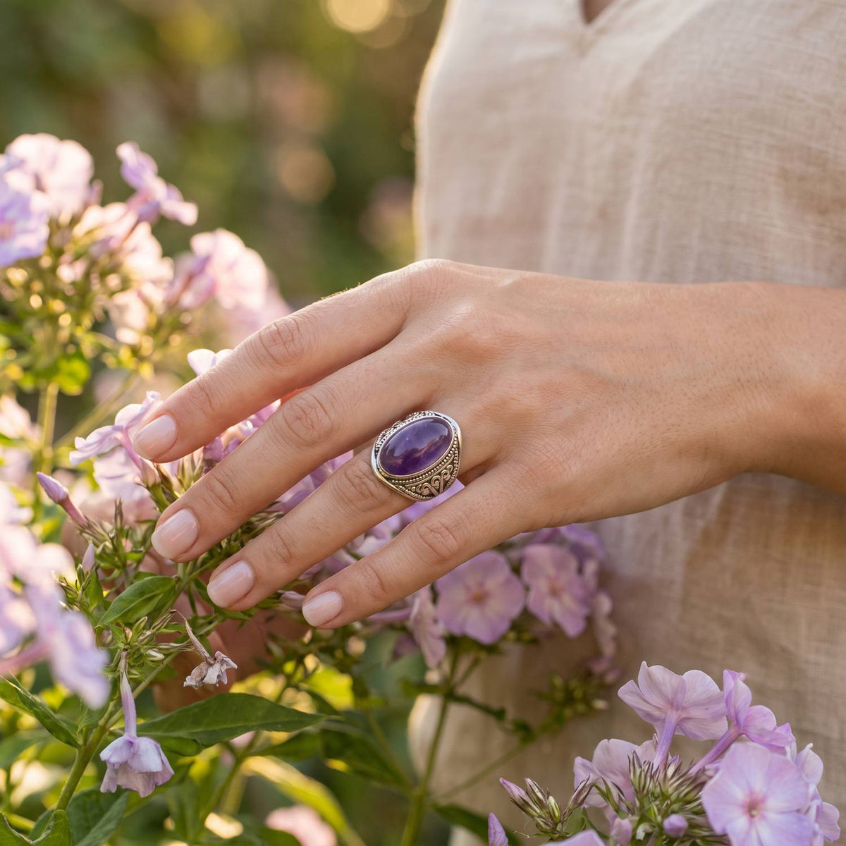 Silberring mit Amethyst an der Hand zwischen Blumen
