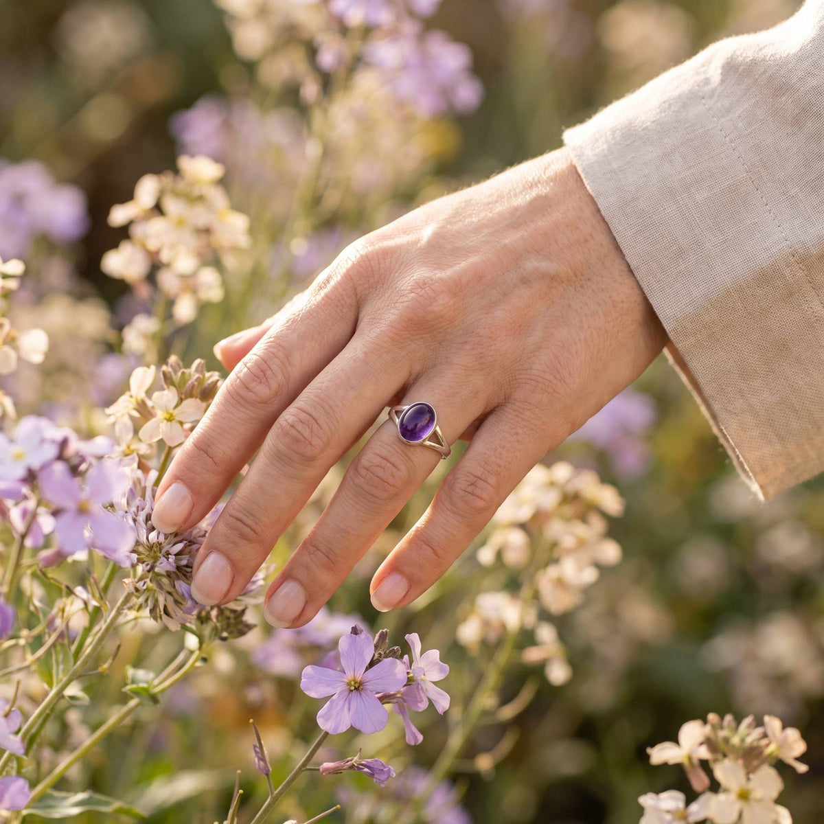 Silberring mit Amethyst an der Hand zwischen Blumen
