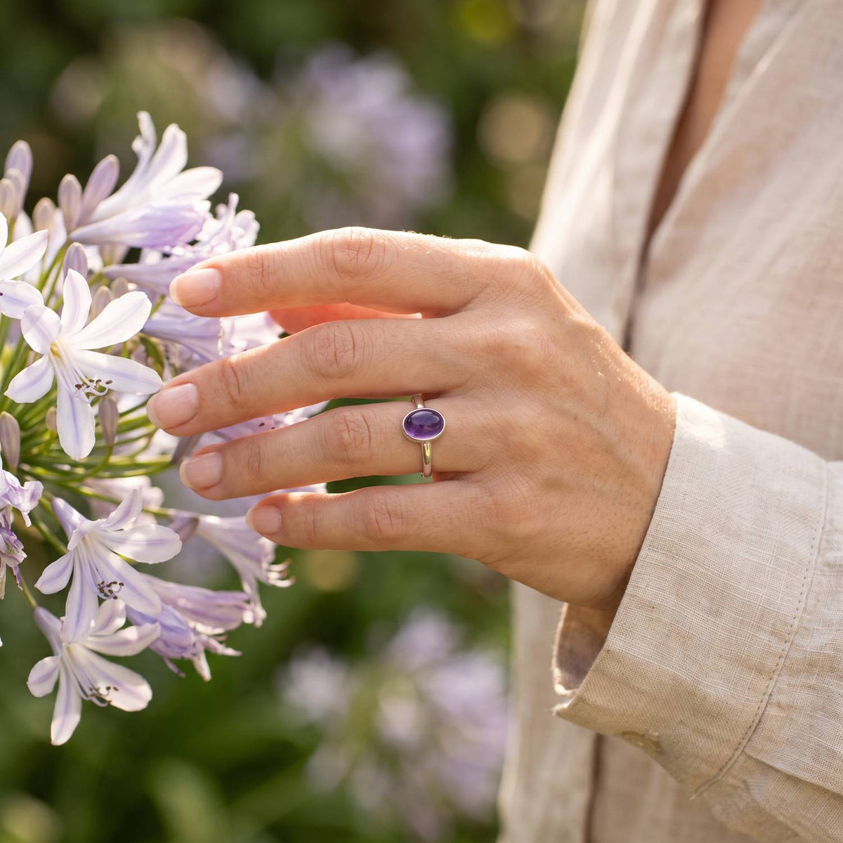 Silberring mit Amethyst an der Hand zwischen Blumen