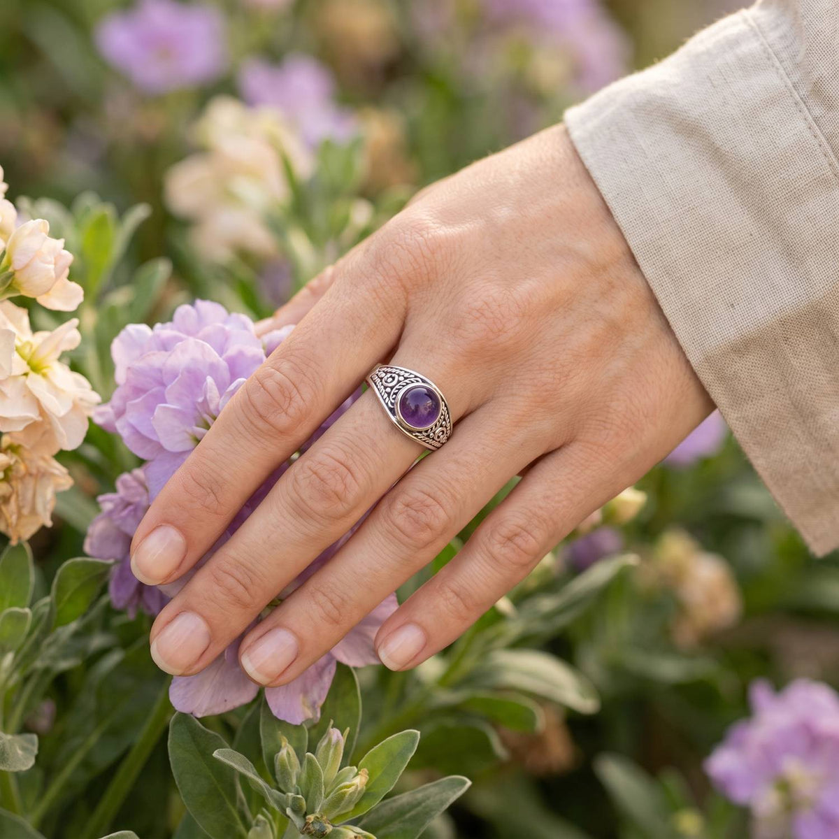 Silberring mit Amethyst an der Hand zwischen Blumen