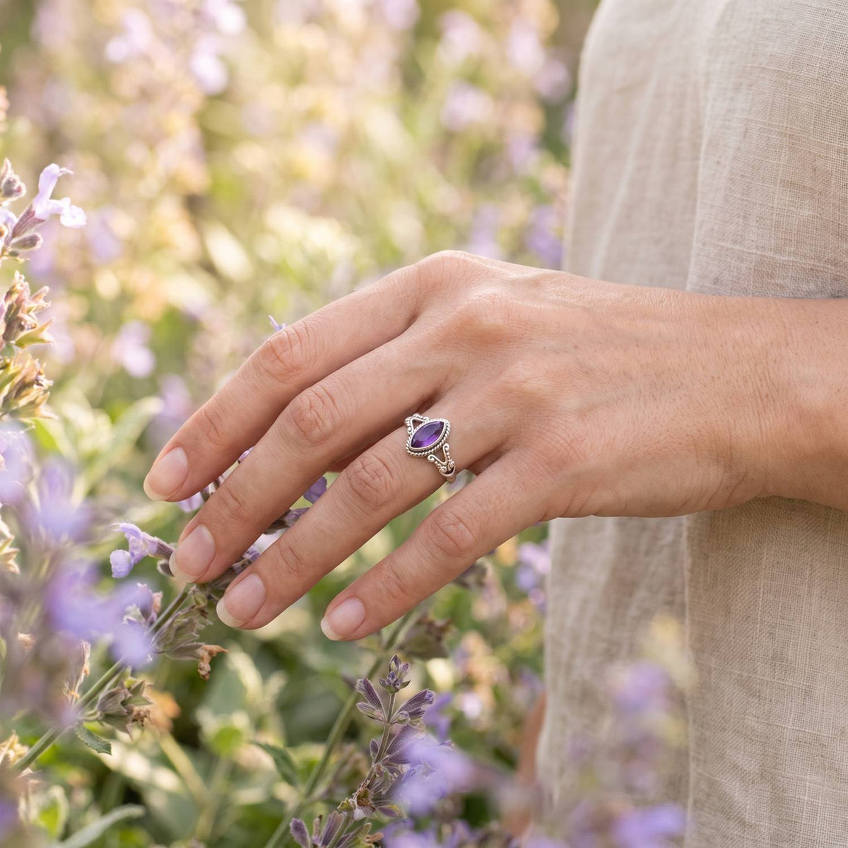 Silberring mit Amethyst an der Hand zwischen Blumen