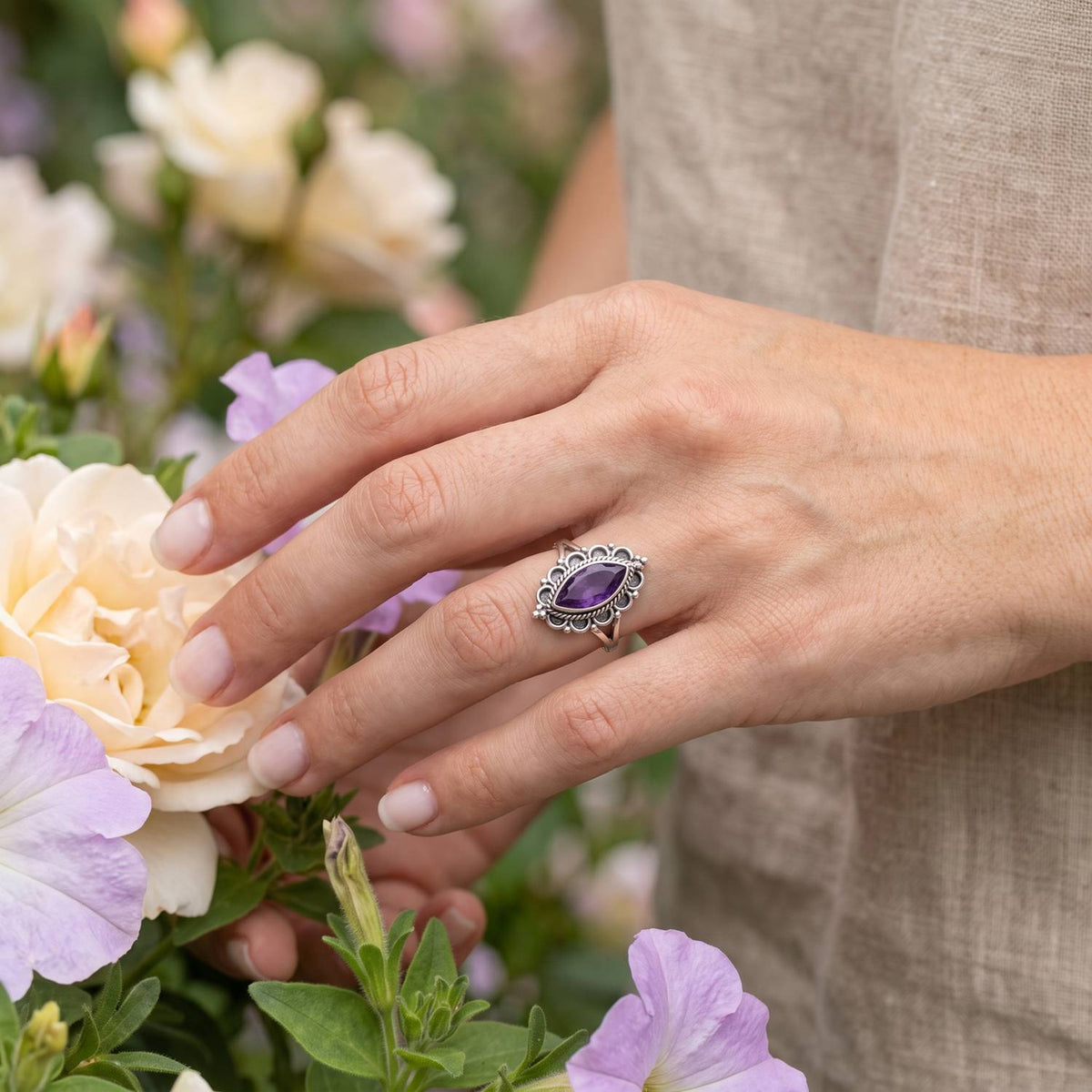 Silberring mit Amethyst an der Hand zwischen Blumen