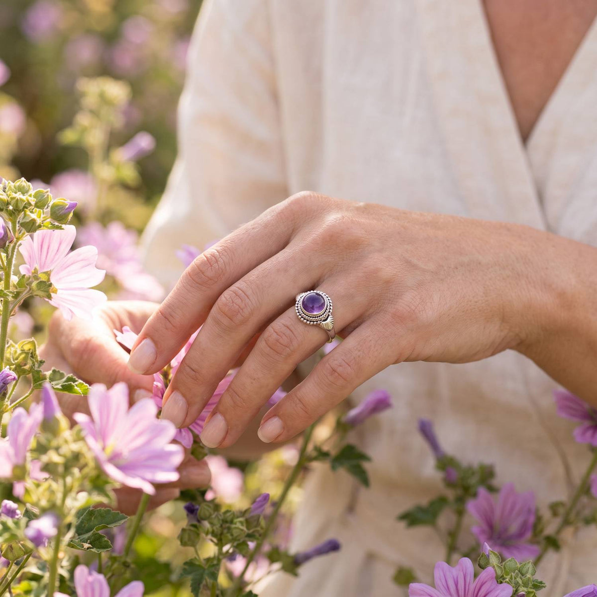 Silberring mit Amethyst an der Hand zwischen Blumen