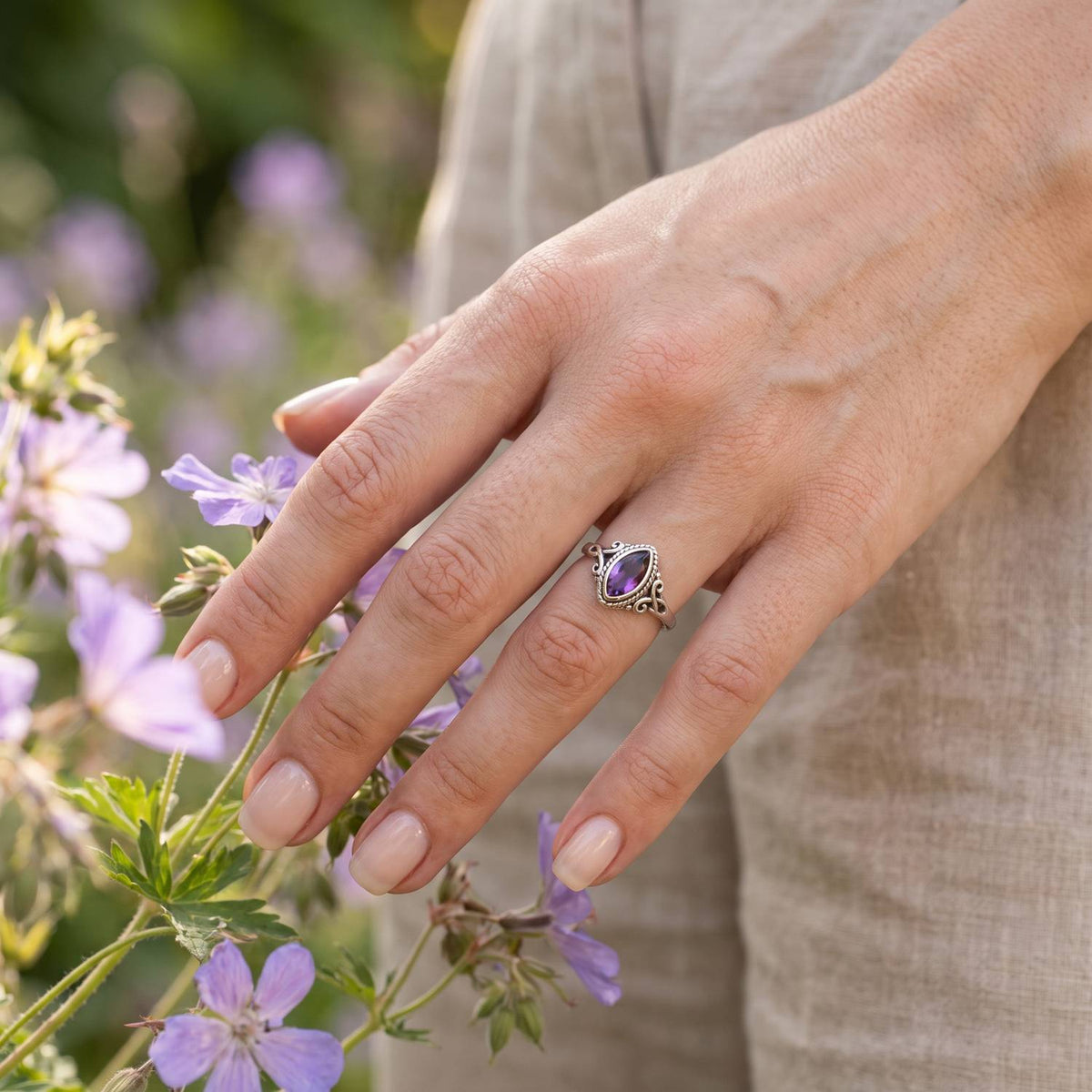 Silberring mit Amethyst an der Hand zwischen Blumen