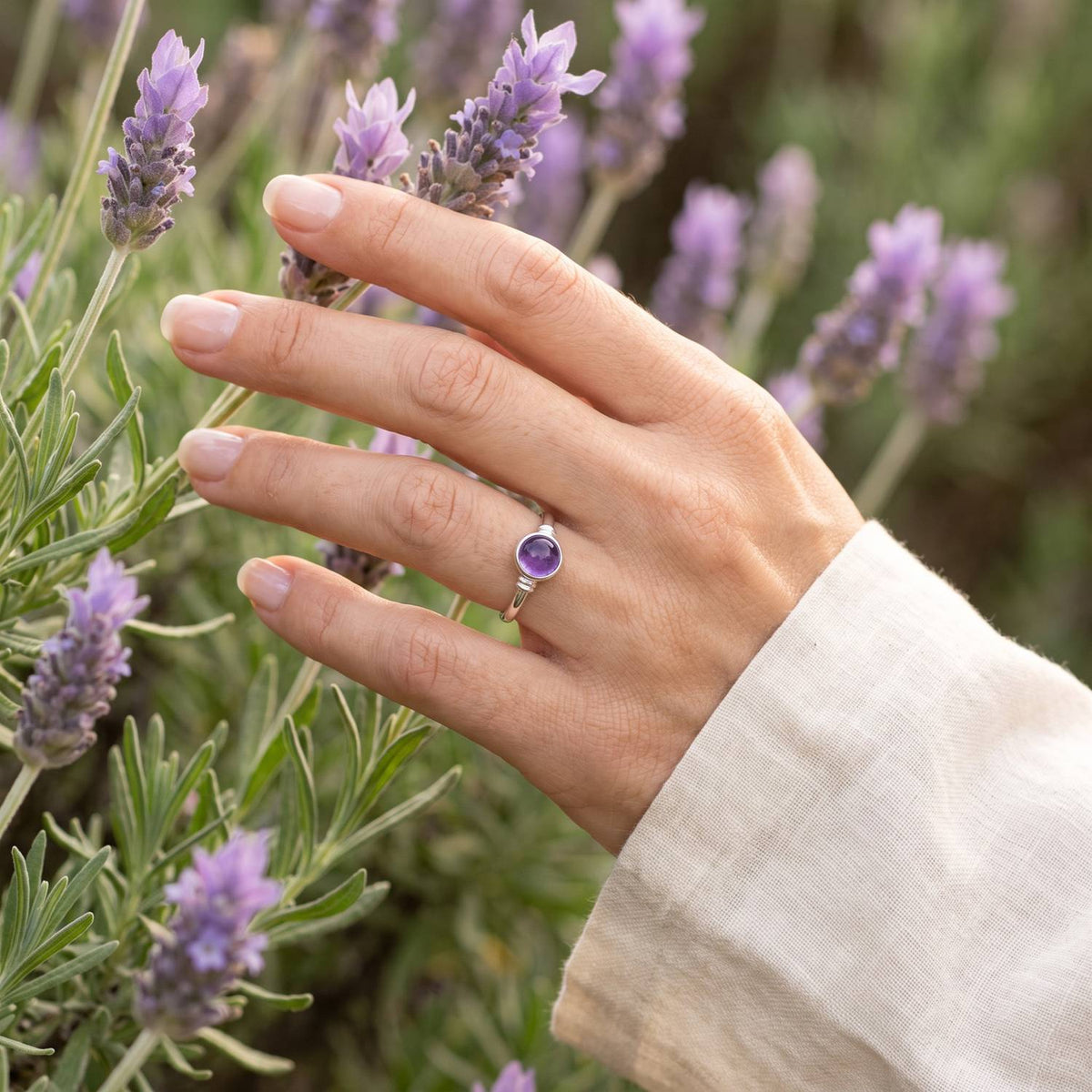 Silberring mit Amethyst an der Hand zwischen Blumen