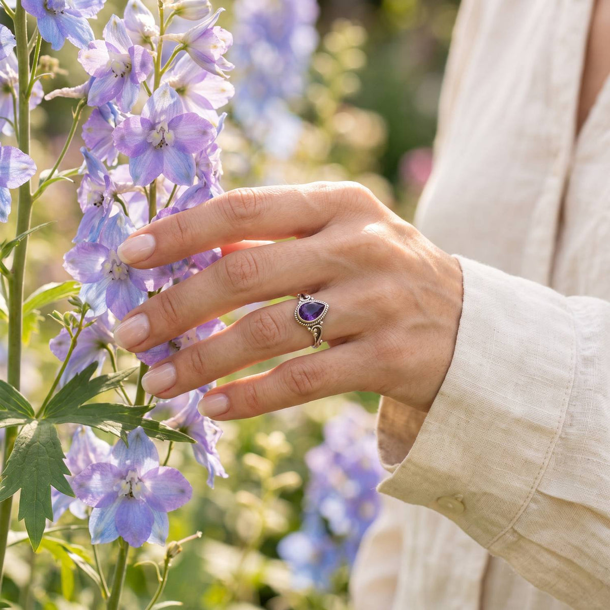 Silberring mit Amethyst an der Hand zwischen Blumen