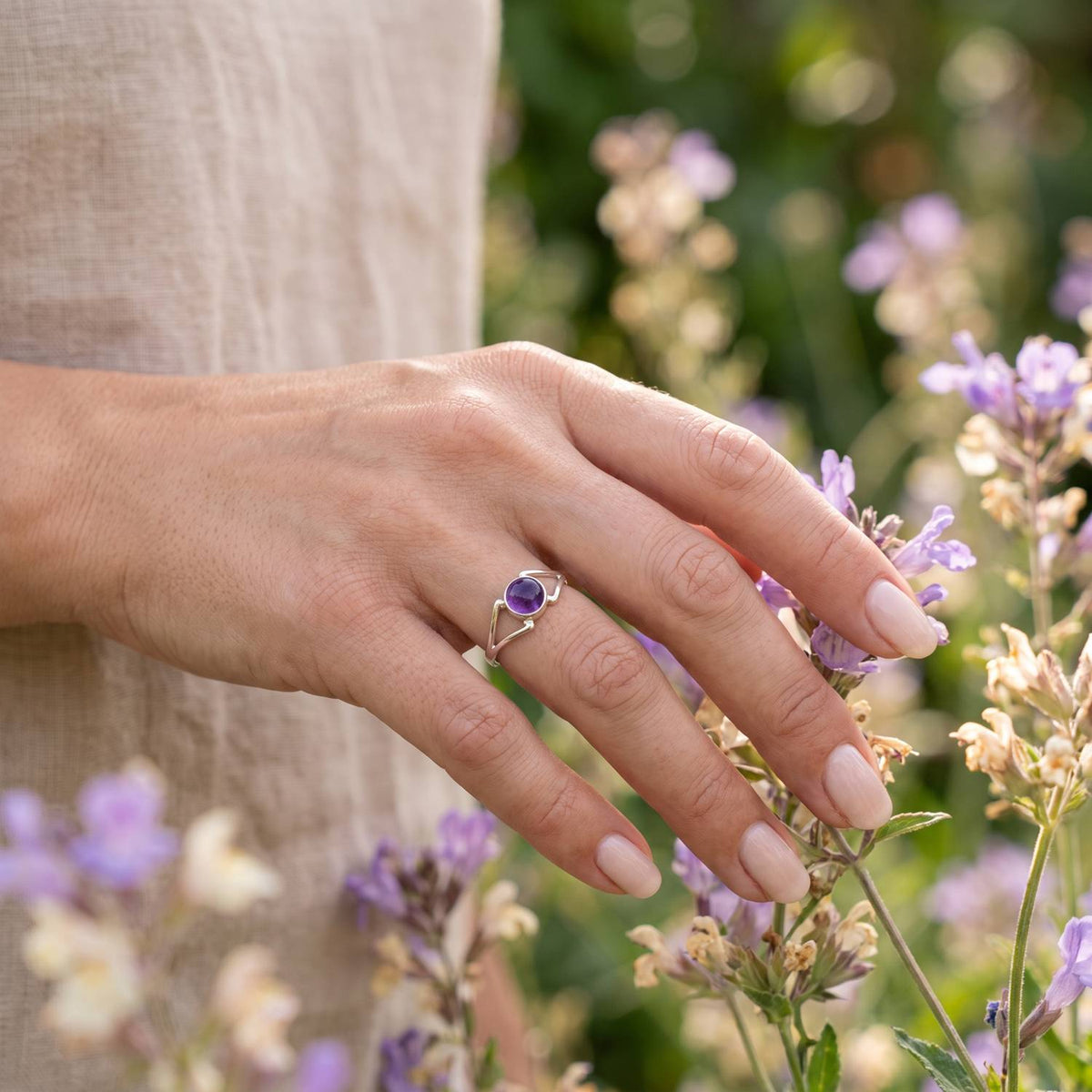 Silberring mit Amethyst an der Hand zwischen Blumen