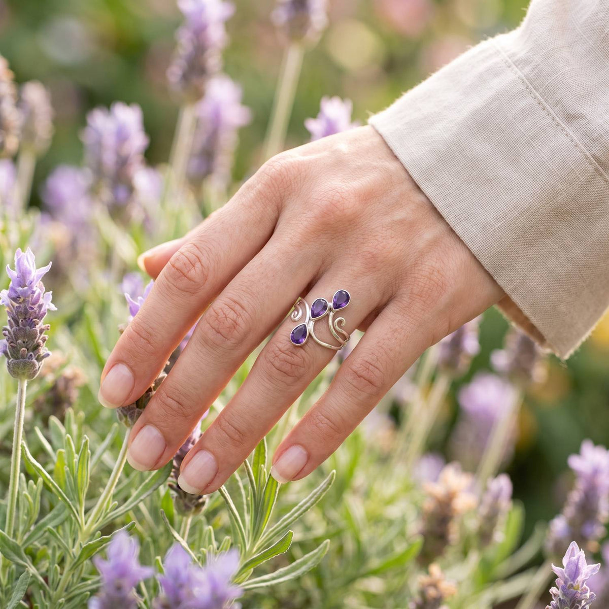 Silberring mit Amethyst an der Hand zwischen Blumen
