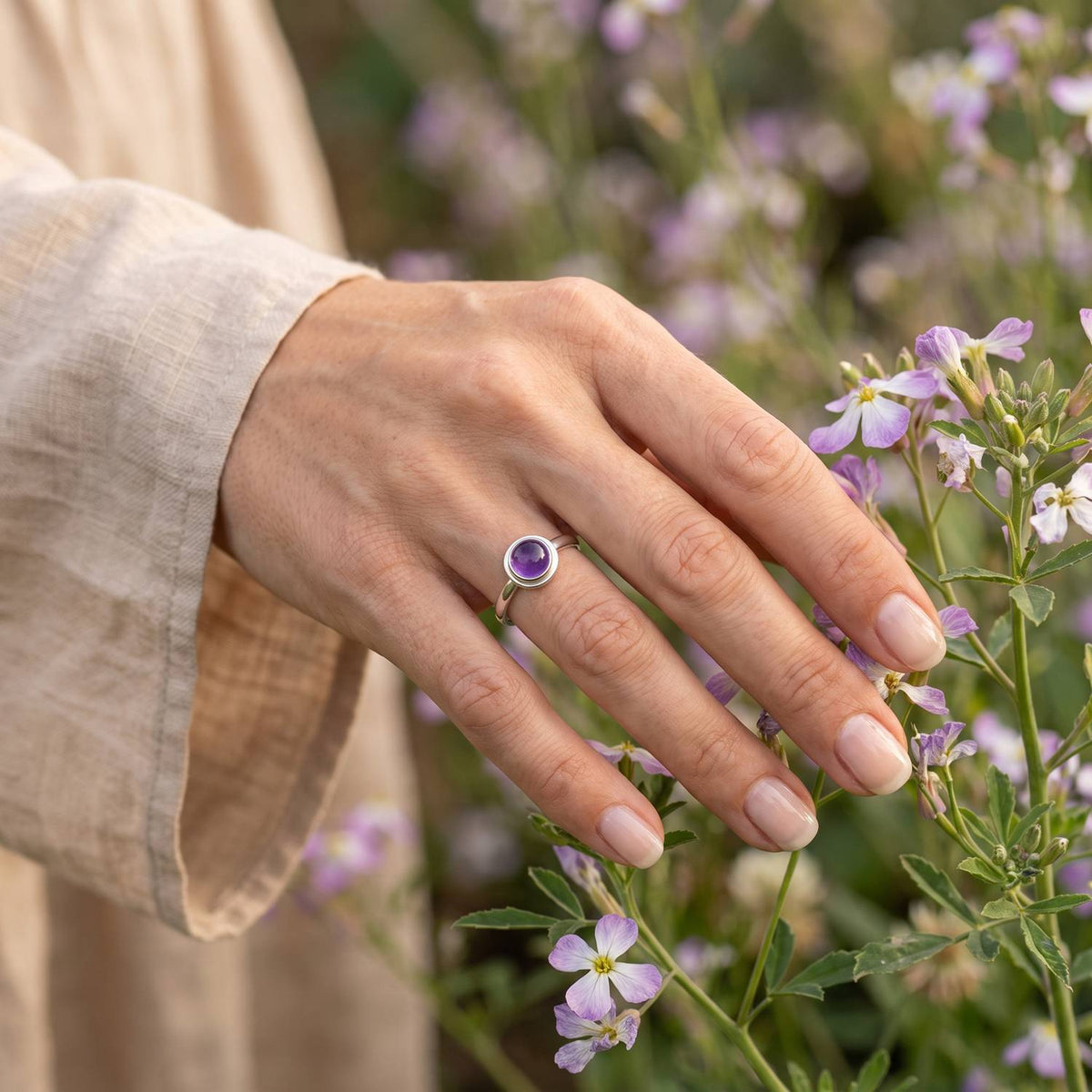 Silberring mit Amethyst an der Hand zwischen Blumen