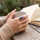 [KI] Amethystring aus Silber getragen beim Lesen mit einer Tasse