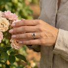 [KI] Silberring mit Granat an der Hand zwischen Blumen