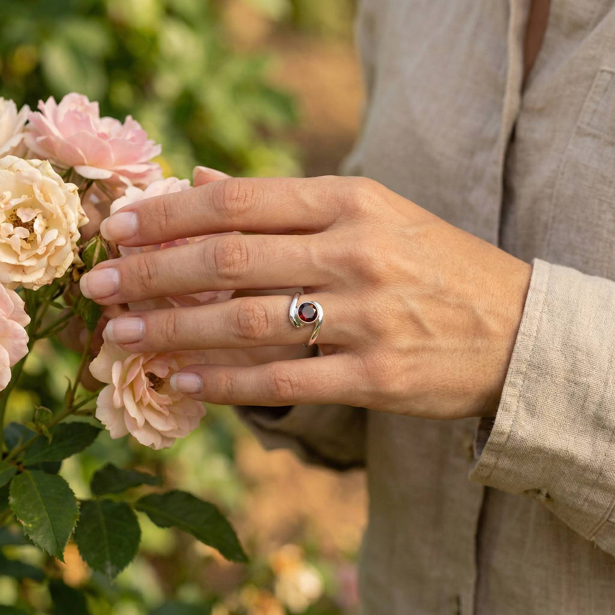 Silberring mit Granat an der Hand zwischen Blumen