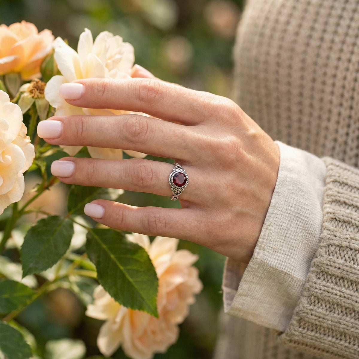Silberring mit Granat an der Hand zwischen Blumen