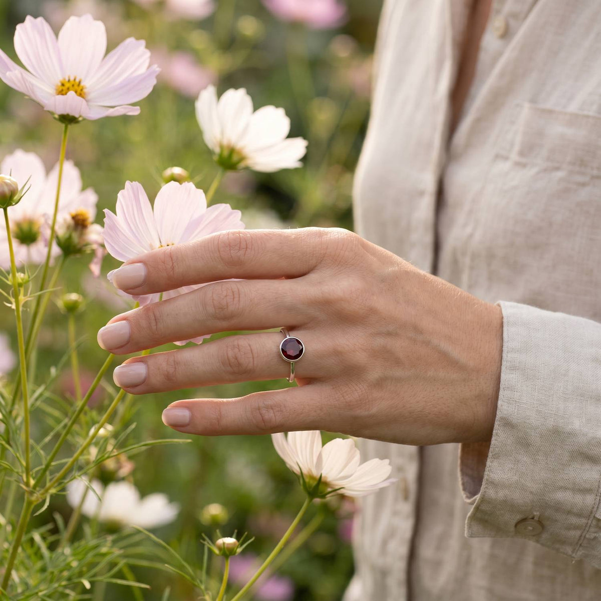 Silberring mit Granat an der Hand zwischen Blumen