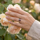 [KI] Silberring mit Granat an der Hand zwischen Blumen