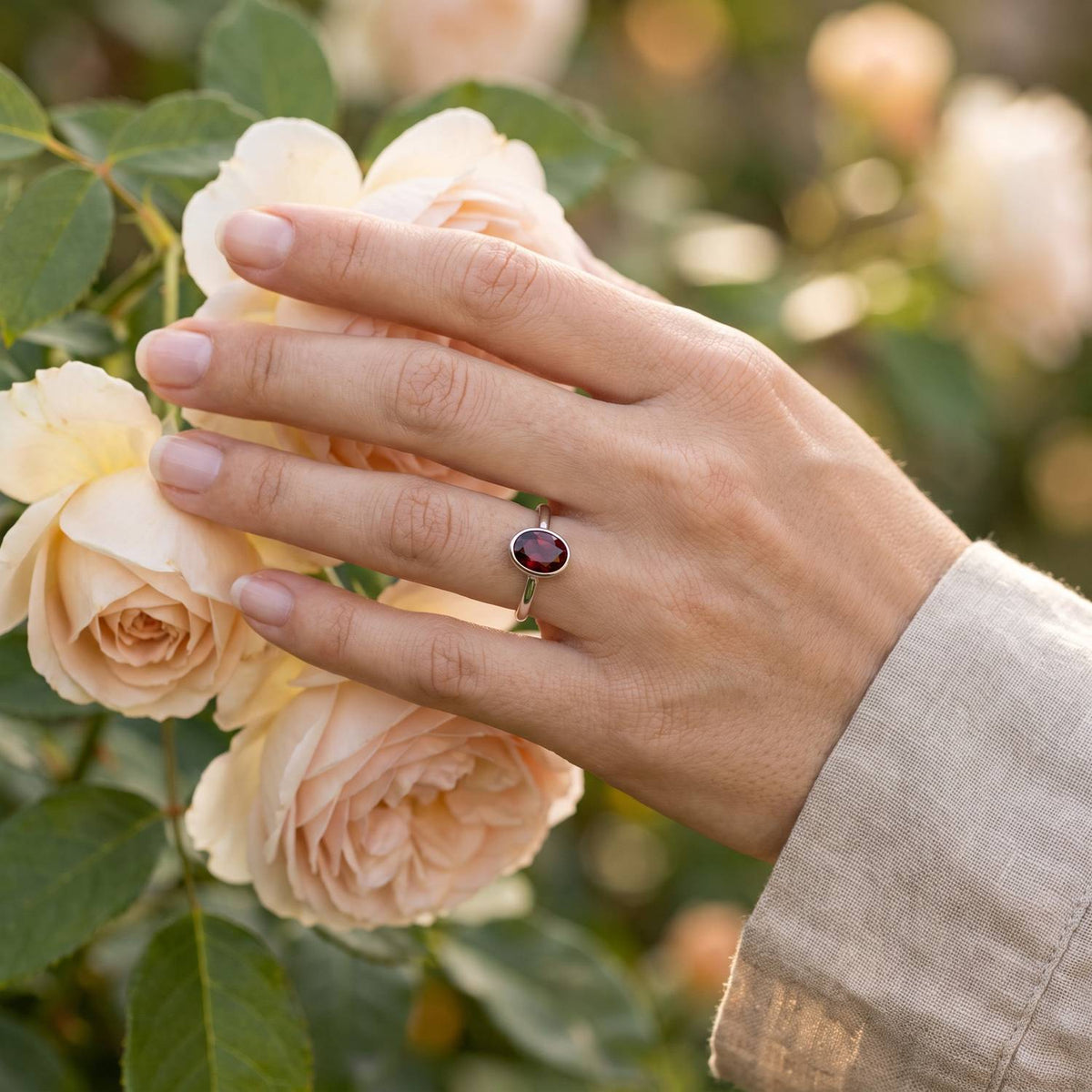 Silberring mit Granat an der Hand zwischen Blumen