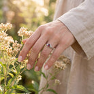 [KI] Silberring mit Granat an der Hand zwischen Blumen