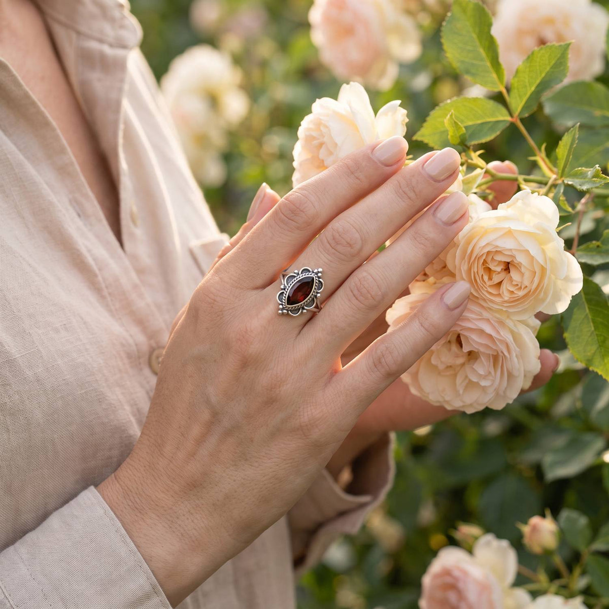 Silberring mit Granat an der Hand zwischen Blumen