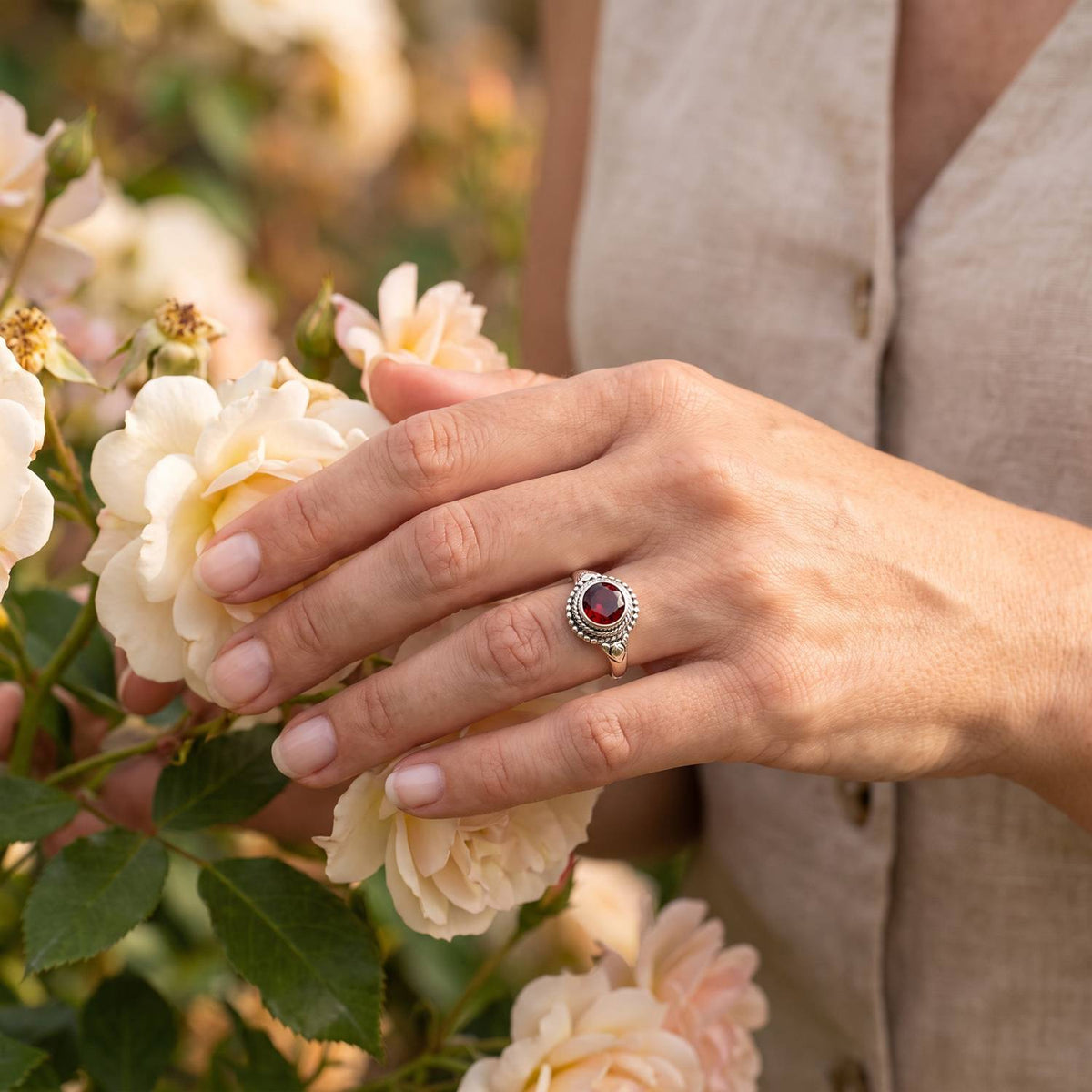 Silberring mit Granat an der Hand zwischen Blumen