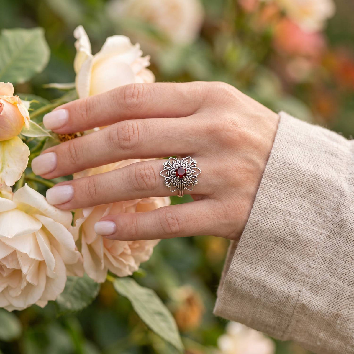 Silberring mit Granat an der Hand zwischen Blumen
