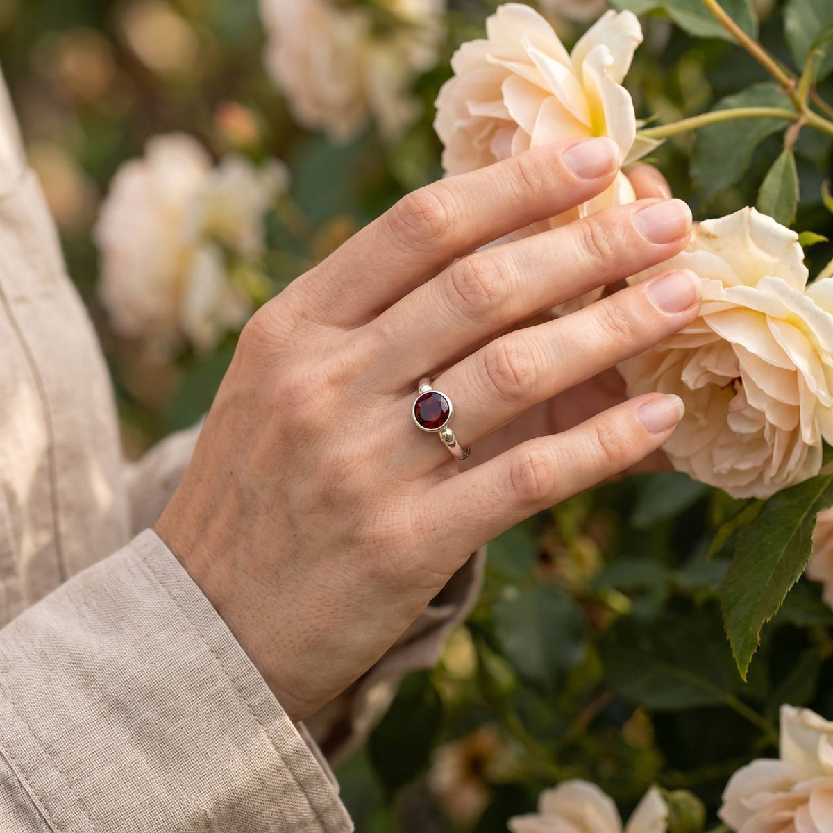 Silberring mit Granat an der Hand zwischen Blumen
