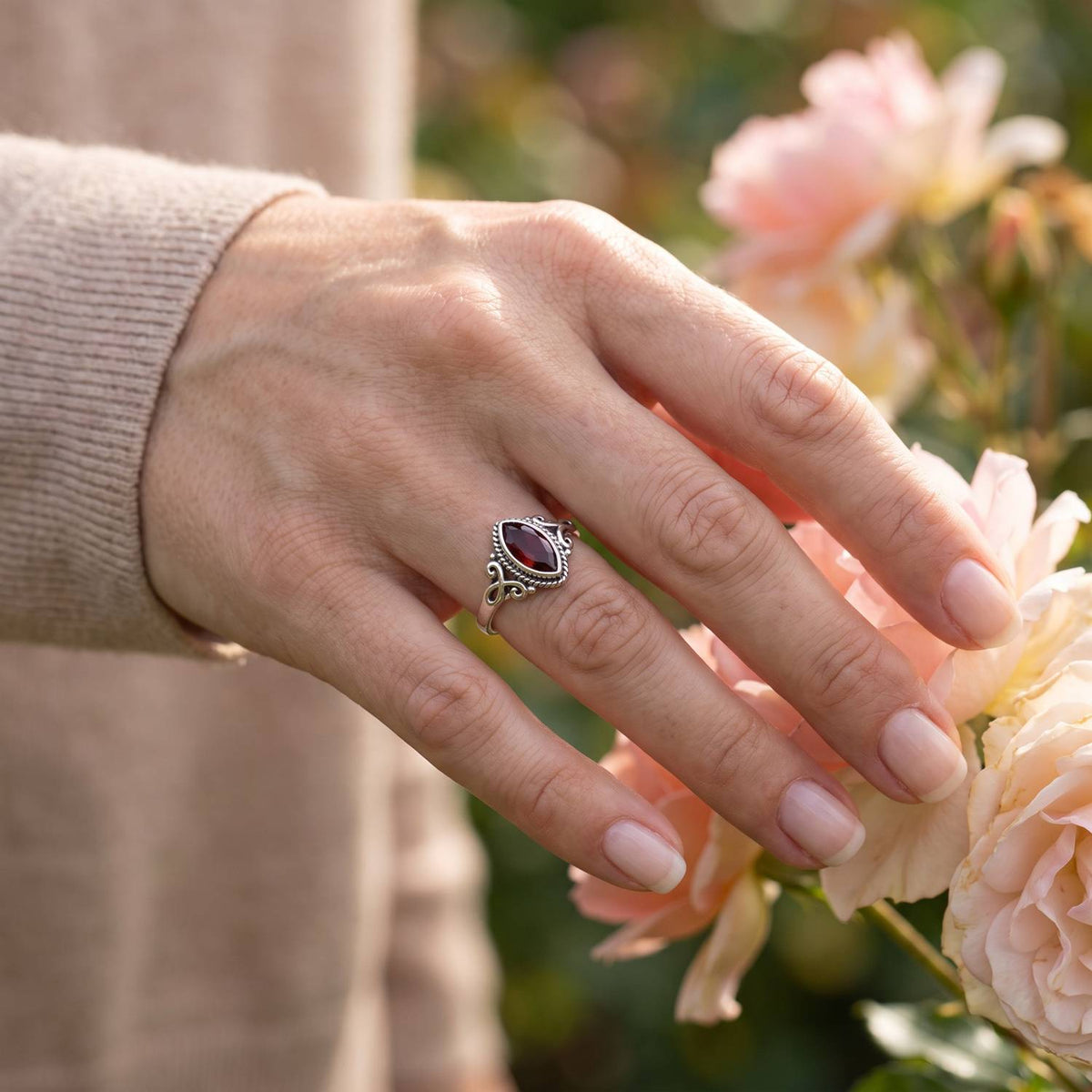 Silberring mit Granat an der Hand zwischen Blumen