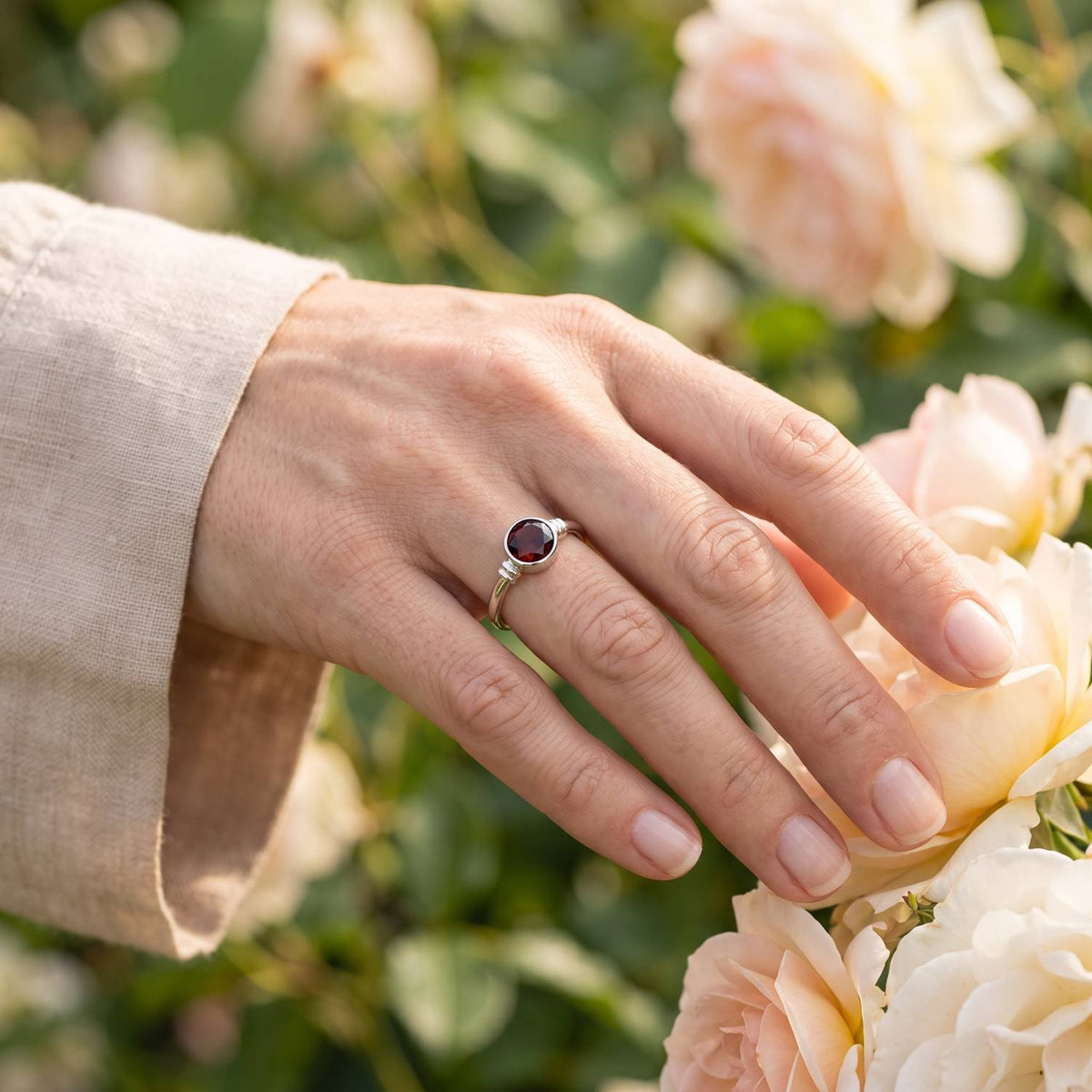 Silberring mit Granat an der Hand zwischen Blumen