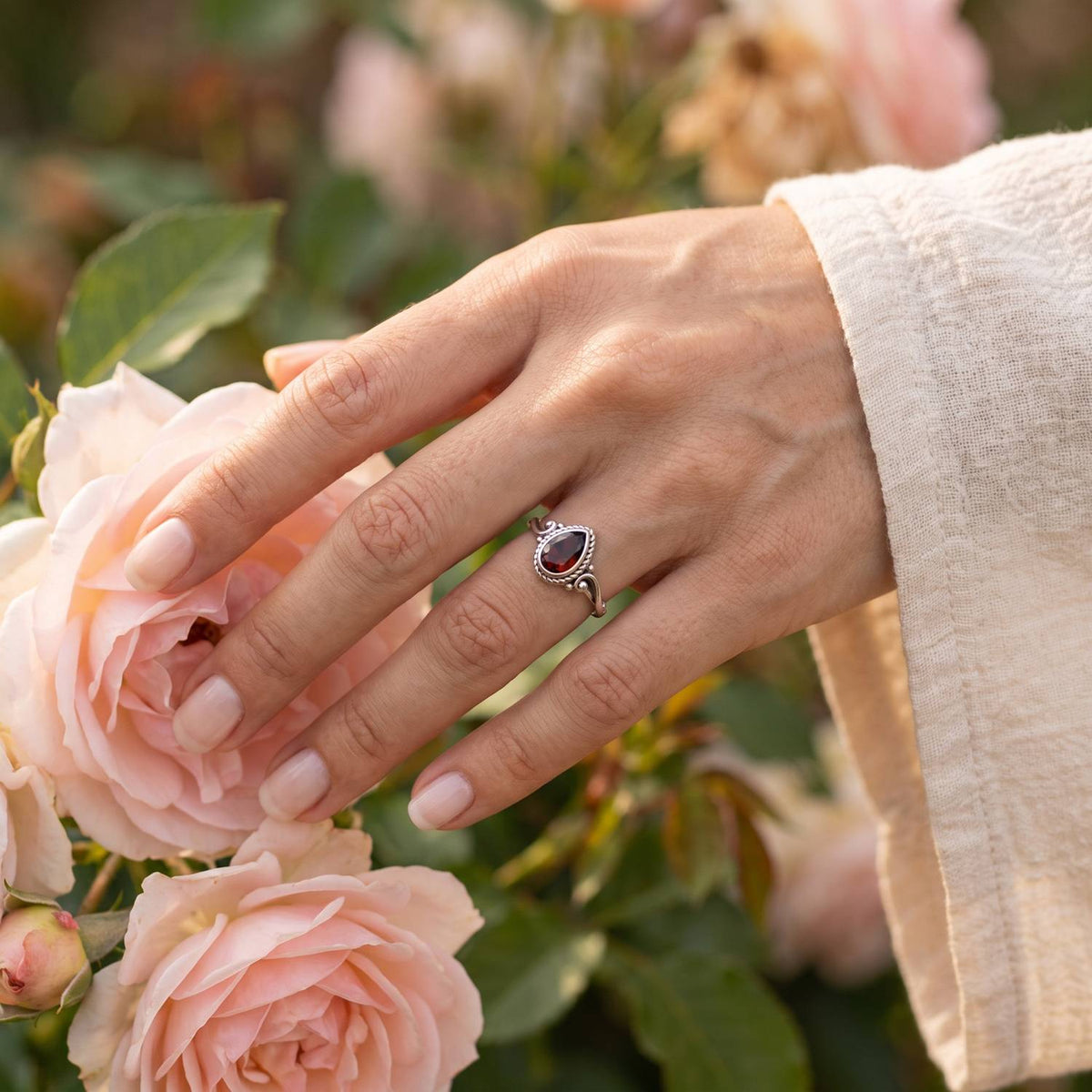 Silberring mit Granat an der Hand zwischen Blumen