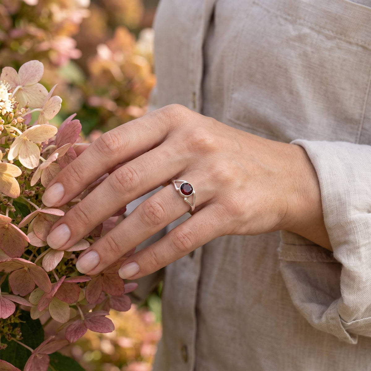Silberring mit Granat an der Hand zwischen Blumen