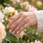 [KI] Silberring mit Granat an der Hand zwischen Blumen