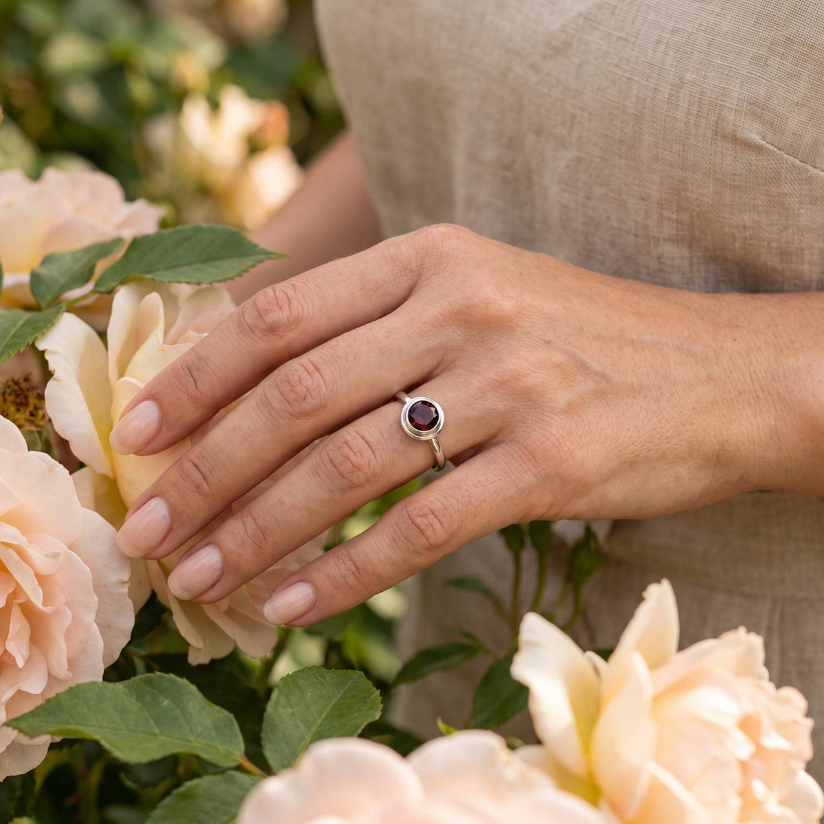 Silberring mit Granat an der Hand zwischen Blumen