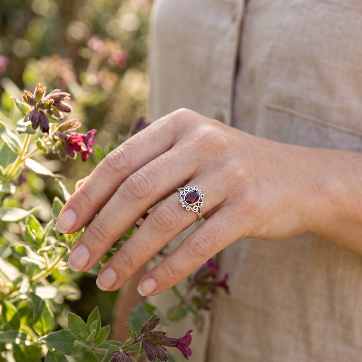 Silberring mit Granat an der Hand zwischen Blumen